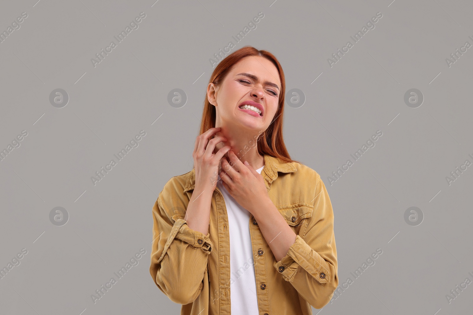 Photo of Suffering from allergy. Young woman scratching her neck on grey background