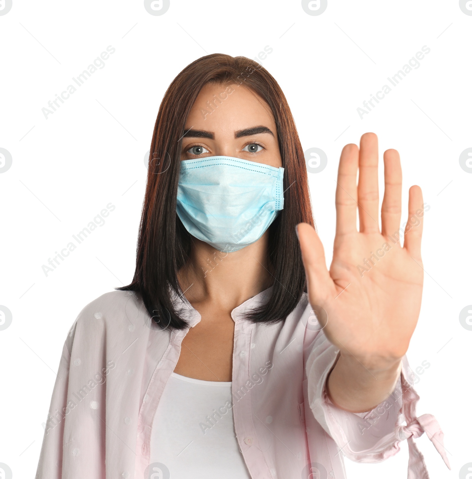 Photo of Young woman in protective mask showing stop gesture on white background. Prevent spreading of coronavirus