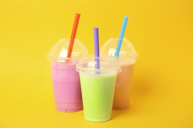 Photo of Plastic cups of tasty milk shakes on color background