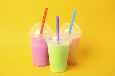 Plastic cups of tasty milk shakes on color background