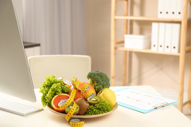 Photo of Nutritionist's workplace with fruits, vegetables and measuring tape on table