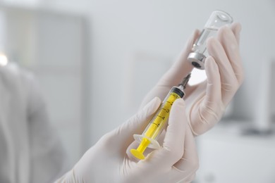 Doctor filling syringe with medication from vial on blurred background, closeup