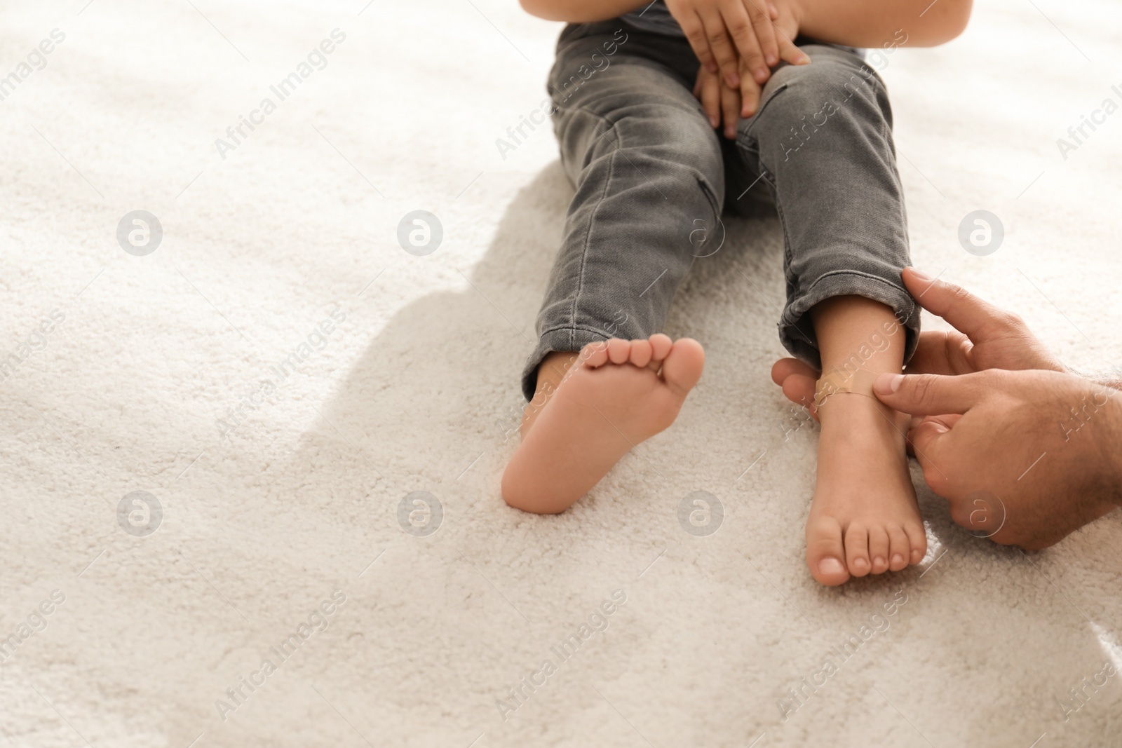 Photo of Father putting sticking plaster onto little son's leg indoors, closeup