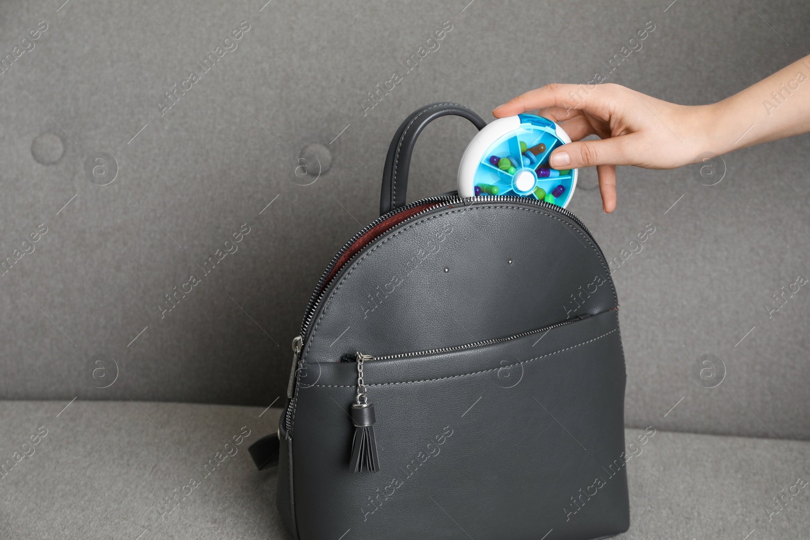 Photo of Woman putting pill box into backpack on sofa, closeup