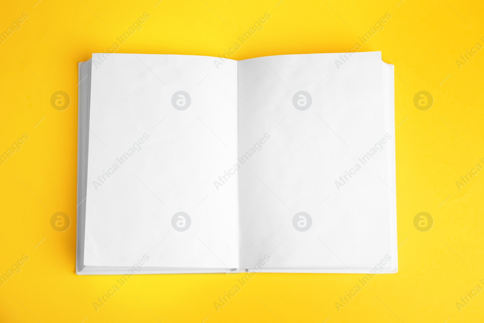 Photo of Open book with blank pages on yellow background, top view