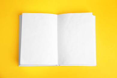 Photo of Open book with blank pages on yellow background, top view