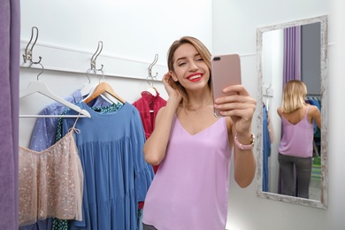 Photo of Young woman taking selfie in dressing room. Fashion store