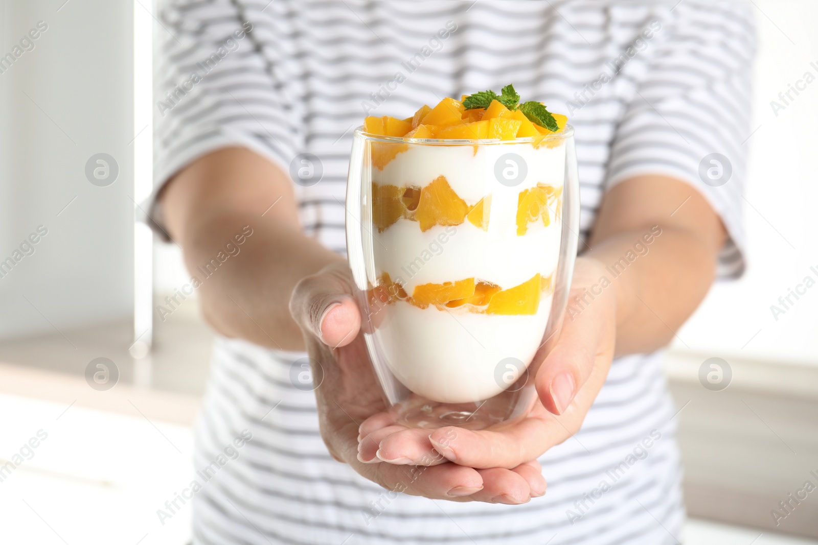 Photo of Woman holding glass of tasty peach dessert with yogurt in kitchen, closeup