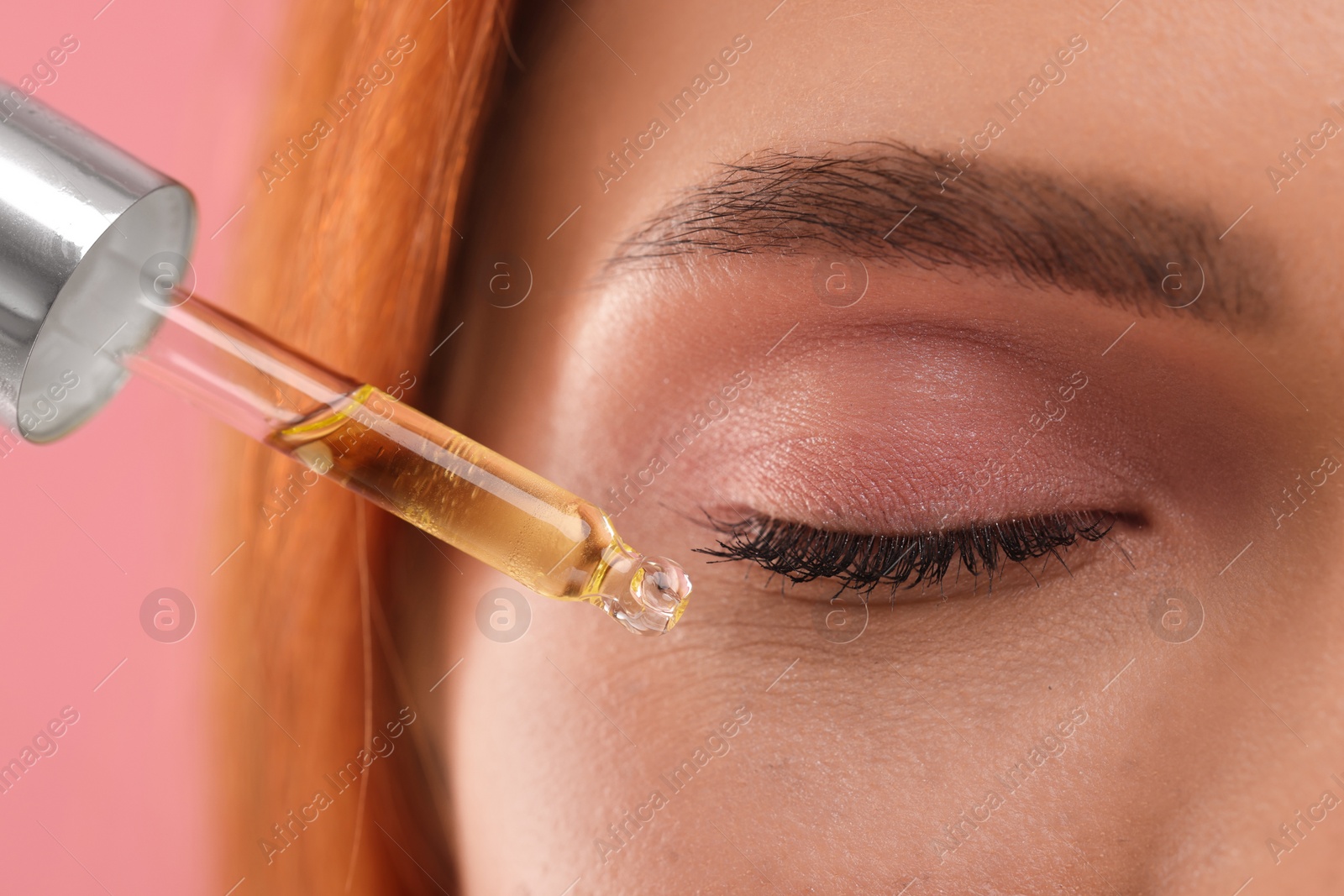 Photo of Beautiful young woman applying cosmetic serum onto her face on pink background, closeup