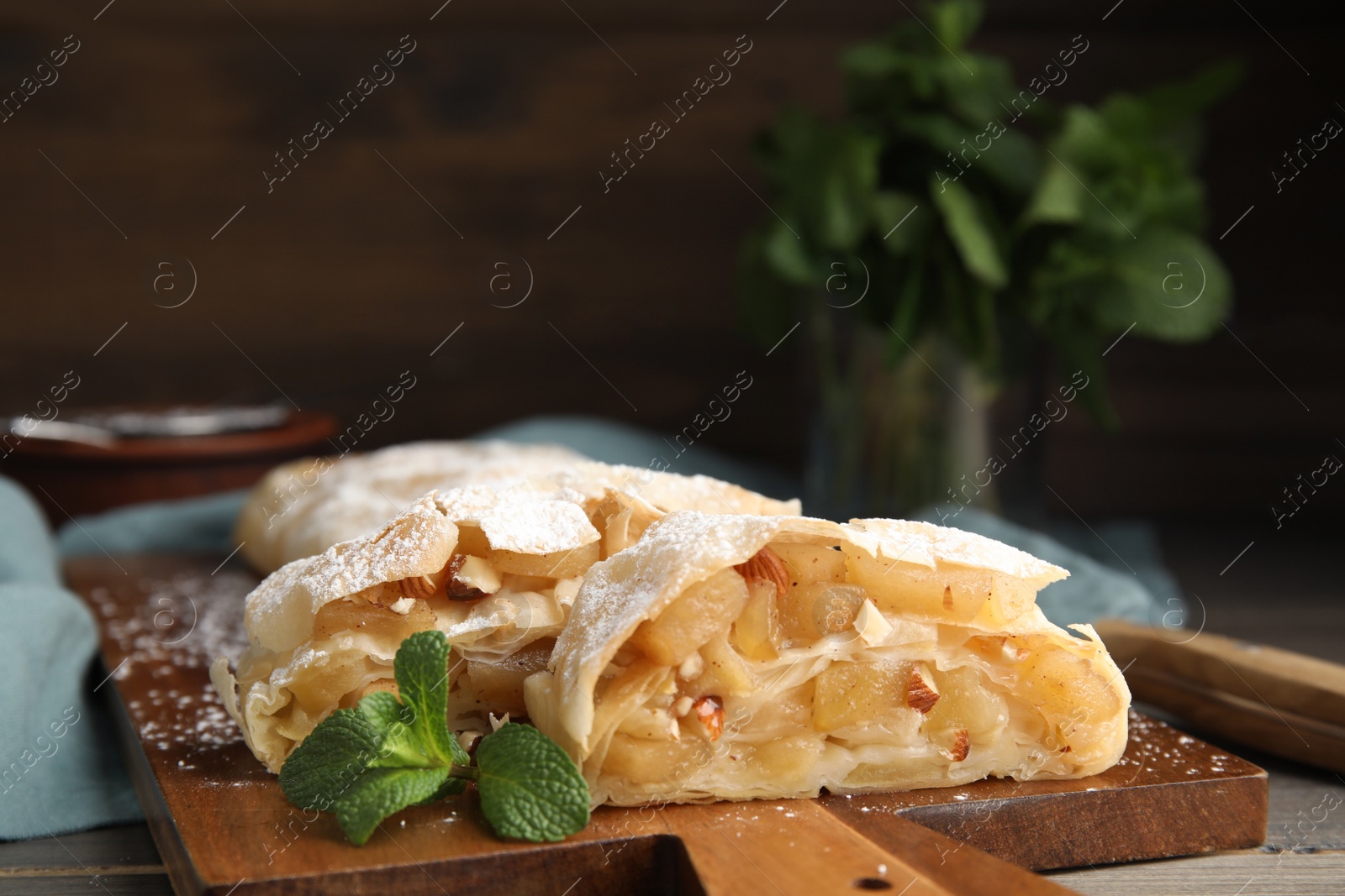 Photo of Delicious apple strudel with almonds, powdered sugar and mint on wooden board, closeup. Space for text