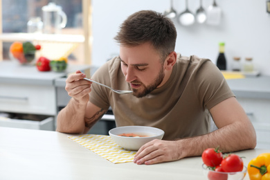 Photo of Young man eating tasty vegetable soup at table in kitchen