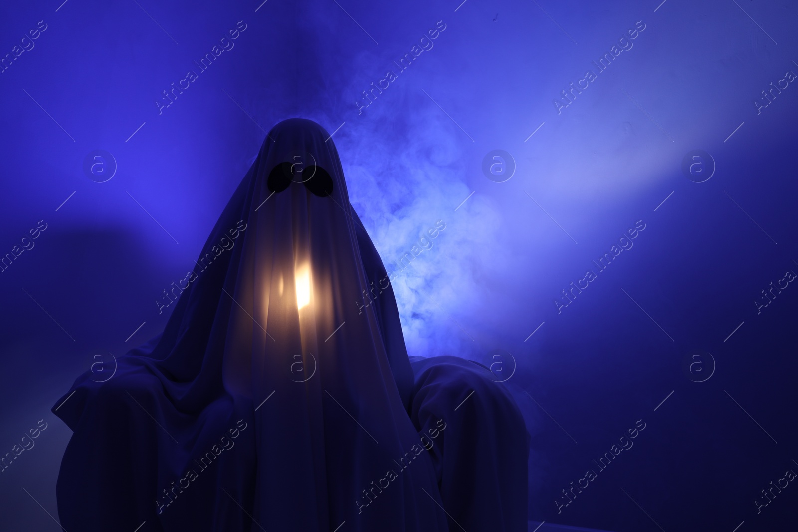 Photo of Creepy ghost. Woman covered with sheet in armchair in blue light, space for text