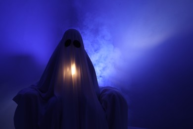 Photo of Creepy ghost. Woman covered with sheet in armchair in blue light, space for text