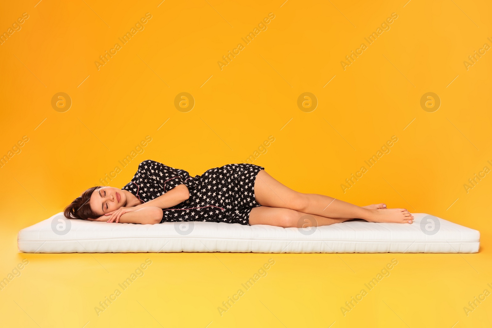 Photo of Young woman sleeping on soft mattress against orange background