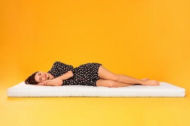 Photo of Young woman sleeping on soft mattress against orange background