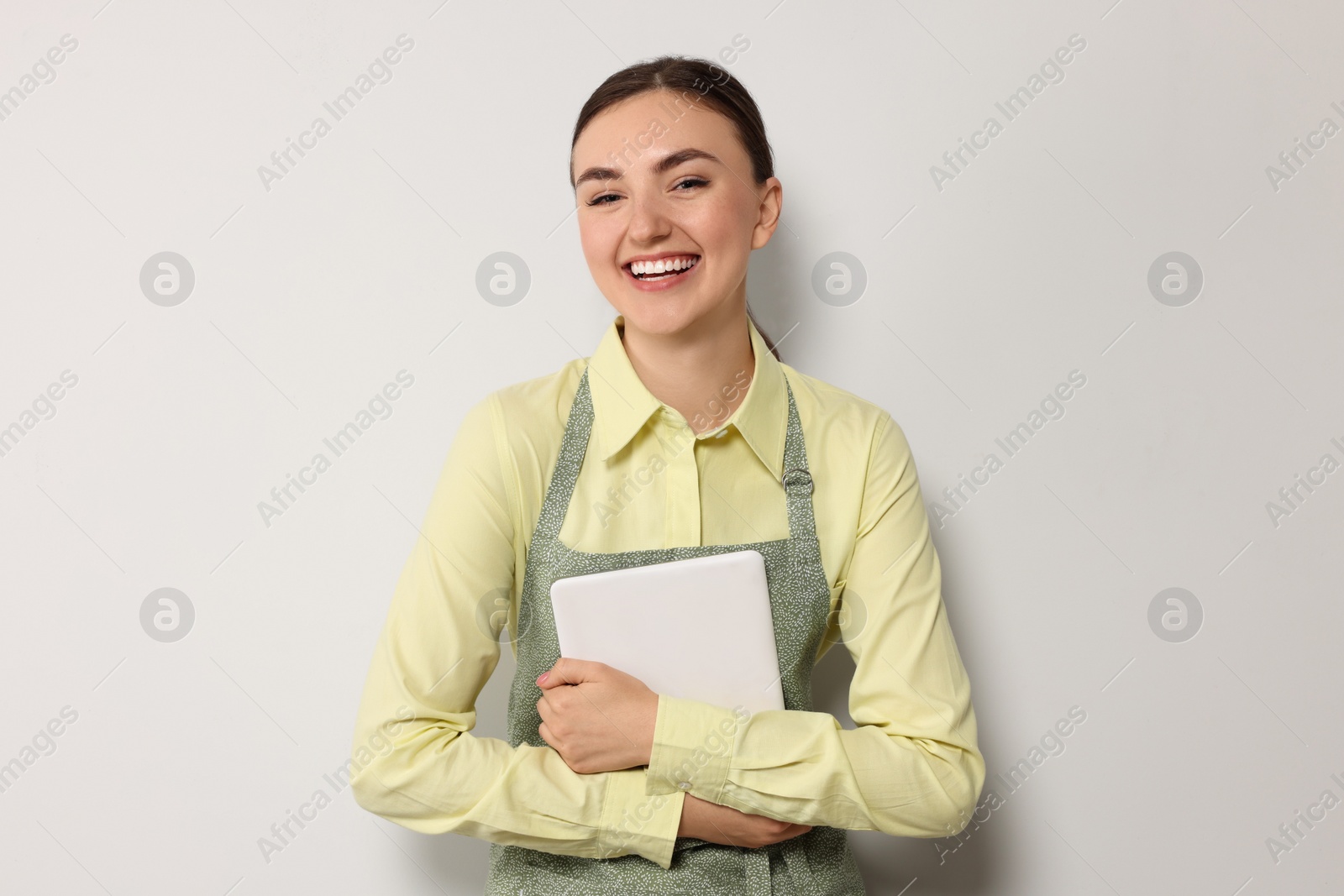 Photo of Beautiful young woman in clean apron with tablet on light grey background