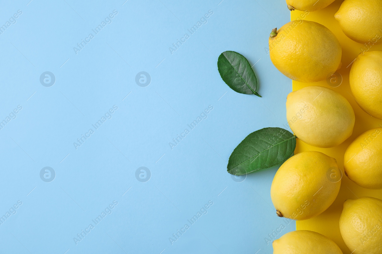 Photo of Ripe fresh lemon fruits and leaves on light blue background, flat lay. Space for text