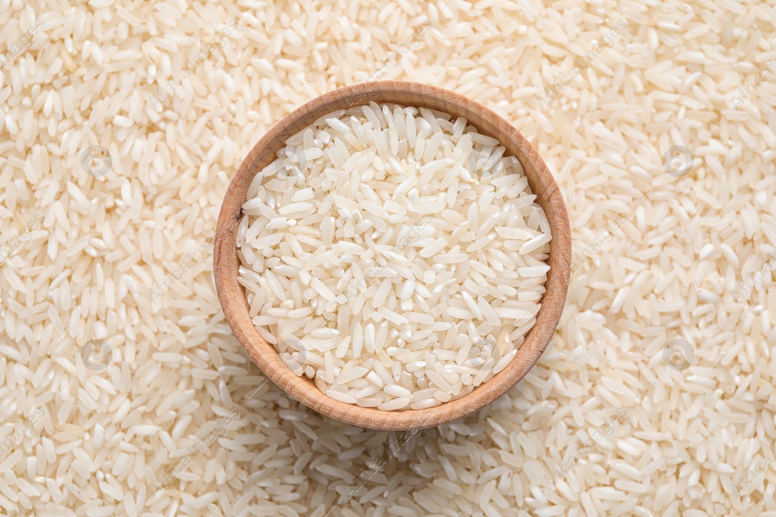 Photo of Pile of polished rice and wooden bowl, top view