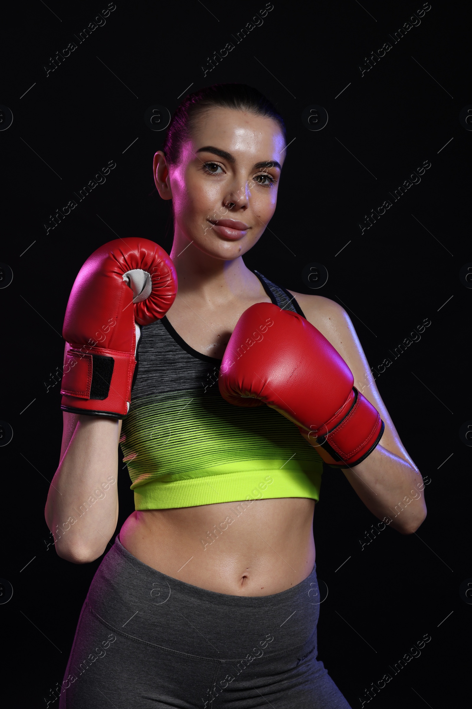 Photo of Portrait of beautiful woman wearing boxing gloves in color lights on black background