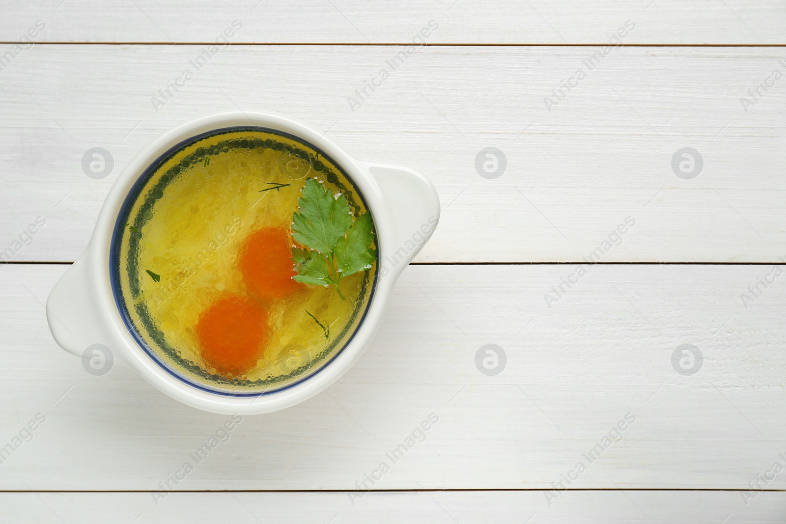 Photo of Delicious chicken bouillon with carrot and parsley on white wooden table, top view. Space for text