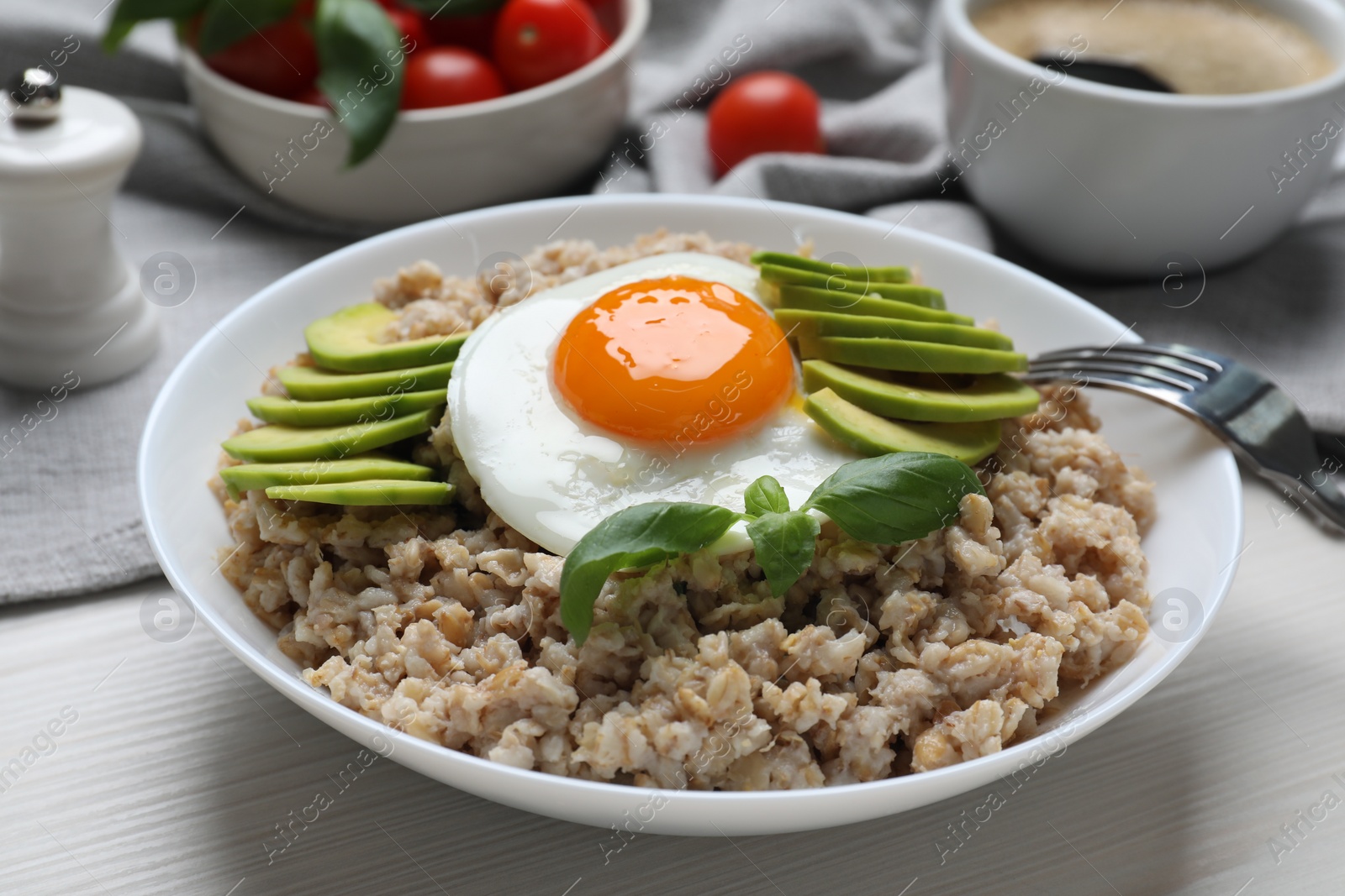 Photo of Delicious boiled oatmeal with fried egg and avocado on white wooden table, closeup