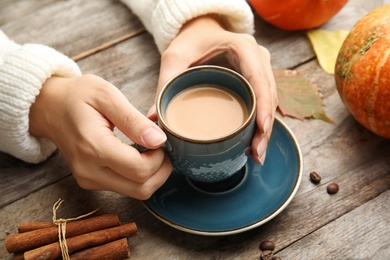 Photo of Woman holding cup with pumpkin spice latte on wooden table