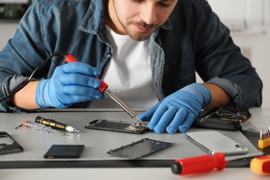 Technician repairing broken smartphone at table, closeup