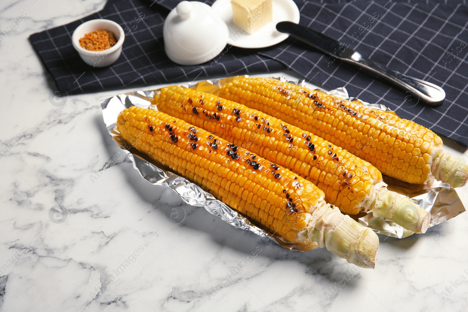 Photo of Fresh grilled tasty corn cobs served with butter on marble table