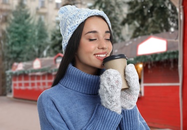 Image of Happy beautiful woman with paper cup of mulled wine at Christmas fair