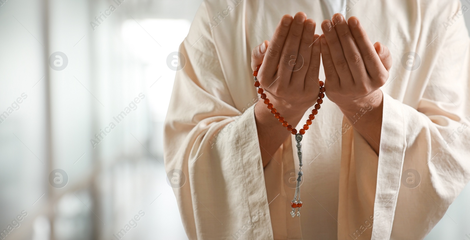 Image of Muslim man with misbaha praying on blurred background, closeup. Banner design with space for text