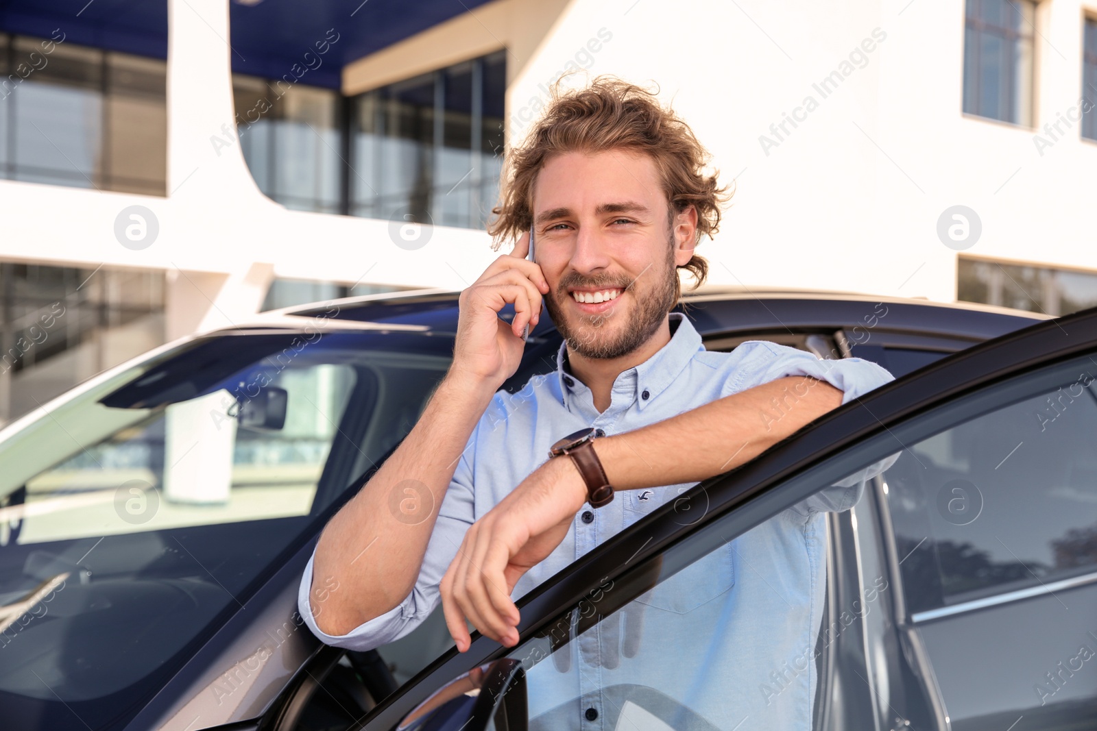 Photo of Young man talking on phone near modern car, outdoors