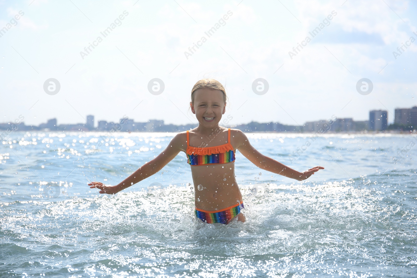 Photo of Happy little girl having fun in sea on sunny day. Beach holiday