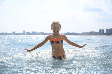 Happy little girl having fun in sea on sunny day. Beach holiday