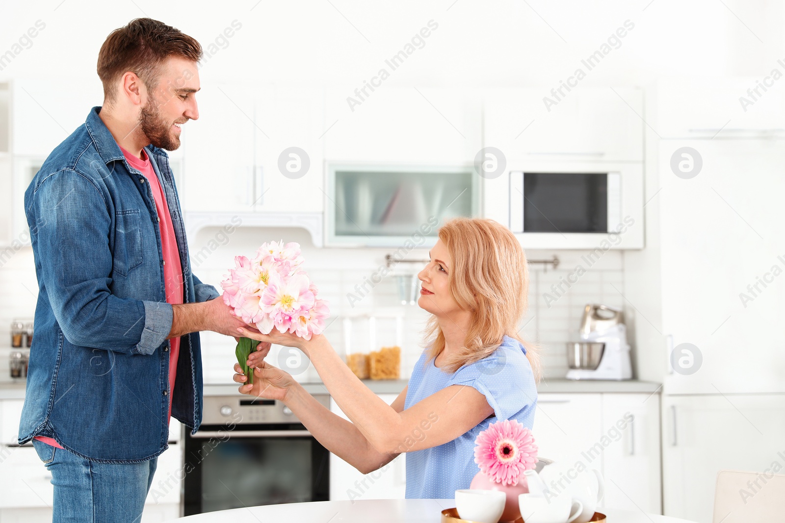 Photo of Young man congratulating his mature mom in kitchen, space for text. Happy Mother's Day