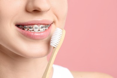 Smiling woman with dental braces and toothbrush on pink background, closeup. Space for text