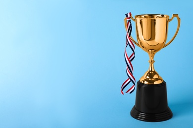 Photo of Golden trophy cup with ribbon on blue background. Space for text