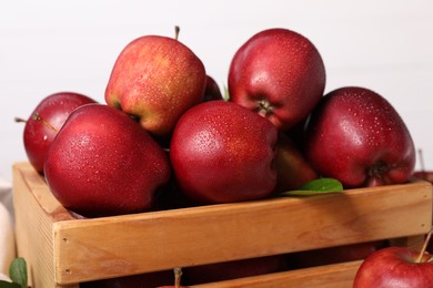 Fresh red apples with water drops in wooden crate on white background, closeup