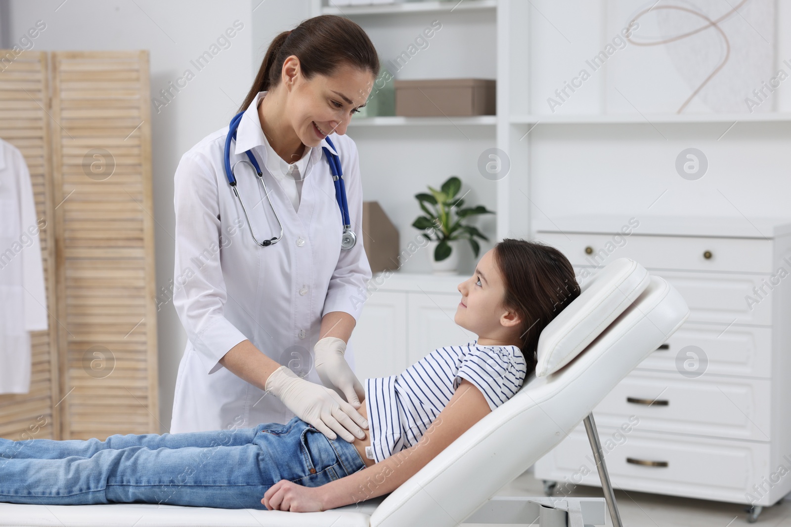 Photo of Gastroenterologist examining girl with stomach ache on couch in clinic