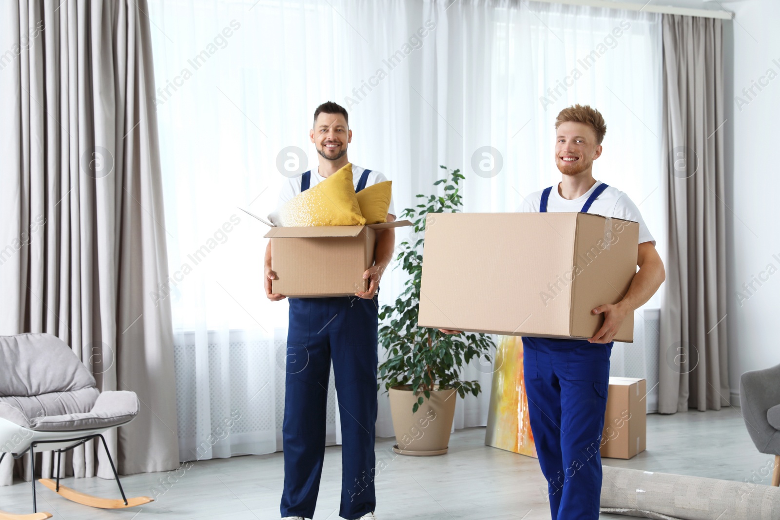 Photo of Moving service employees with cardboard boxes in room