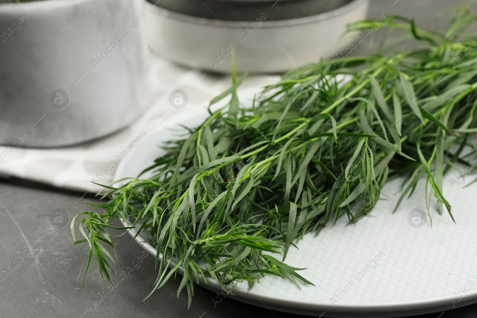 Photo of Plate with fresh tarragon leaves on grey table, closeup