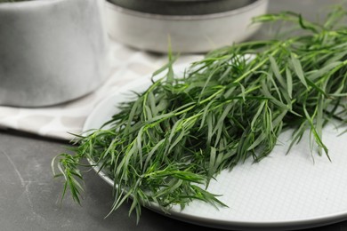 Plate with fresh tarragon leaves on grey table, closeup