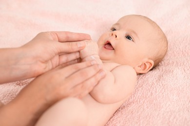 Photo of Woman applying body cream onto baby`s skin on bed, closeup