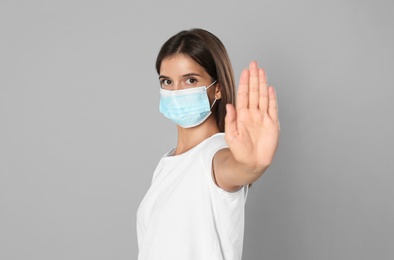 Photo of Woman in protective mask showing stop gesture on grey background. Prevent spreading of coronavirus