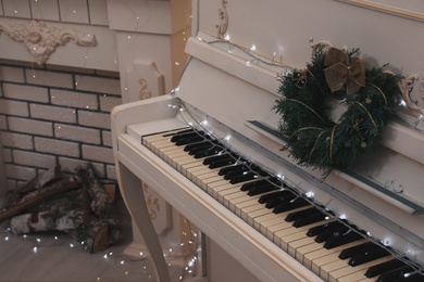 White piano with fairy lights and wreath indoors. Christmas music