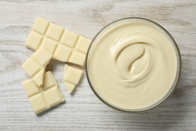 Photo of Tasty white chocolate paste in bowl and pieces on light wooden table, top view