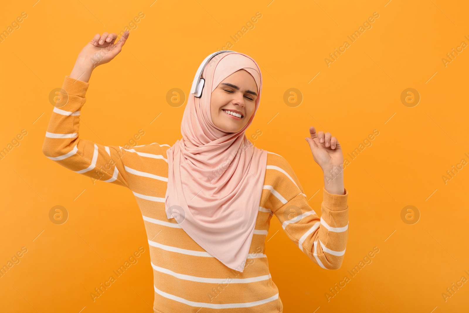 Photo of Muslim woman in hijab and headphones dancing on orange background