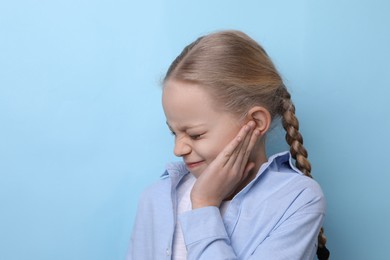 Photo of Cute little girl suffering from ear pain on light blue background