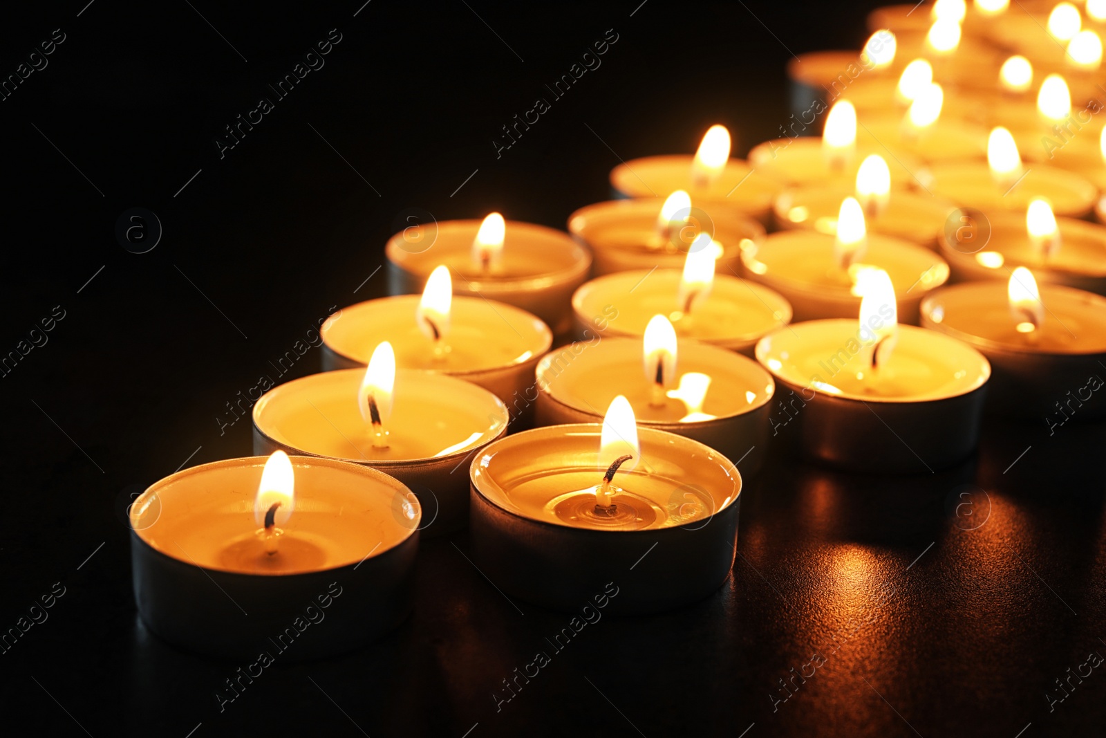 Photo of Wax candles burning on table in darkness, closeup