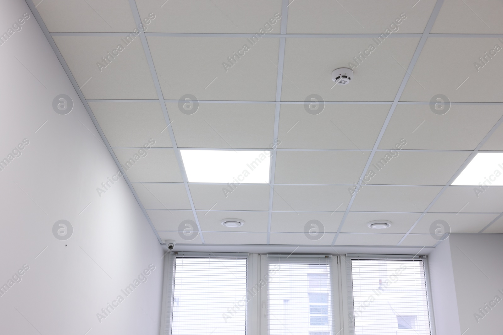 Photo of White ceiling with PVC tiles and lighting indoors, low angle view