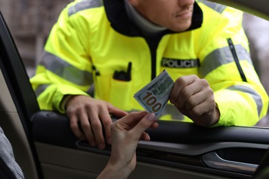 Photo of Woman giving bribe to police officer out of car window, closeup